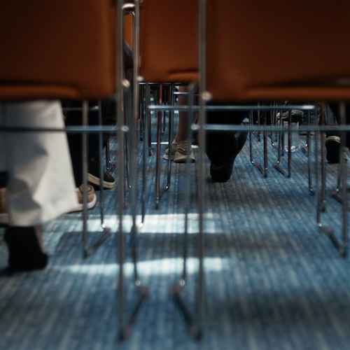 Reihen von Stühlen und menschlichen Beinen auf Bodenhöhe fotografiert